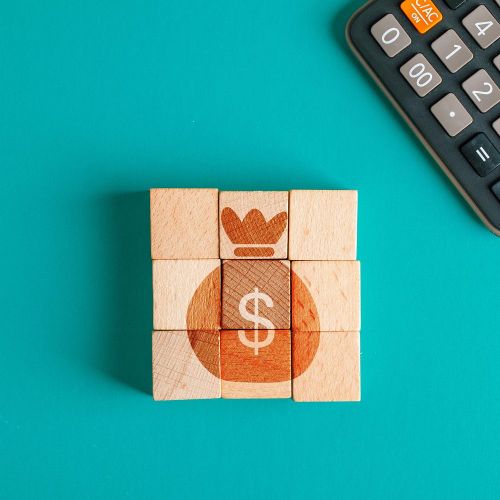 Financial concept with icon on wooden cubes, calculator on turquoise background flat lay.
